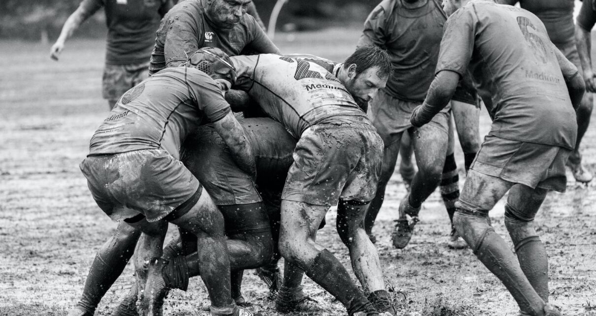 grayscale photography of group of people playing rugby on muddy field